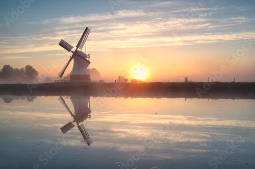 Fototapeta Dutch windmill reflected in river at sunrise