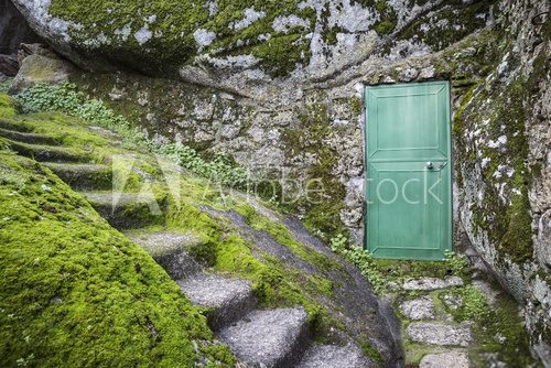 Fototapeta a green metallic door on a big stone and a stairway carved in stone with moss