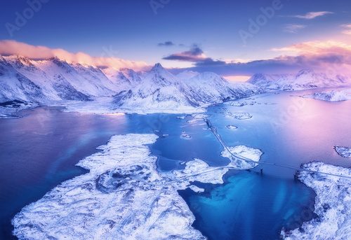 Fototapeta Aerial view of sea, snowy islands, mountains, road, violet sky at sunset in winter. Lofoten islands, Norway. Landscape with mountains and rocks in snow, water at dusk. Top view from drone. Nature