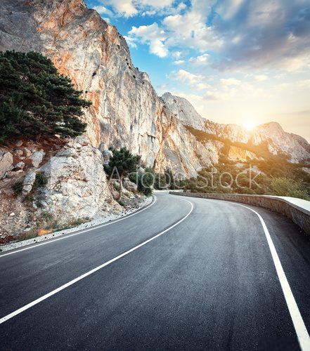 Fototapeta Beautiful winding mountain road with a perfect asphalt with high rocks and colorful sunset in summer. 