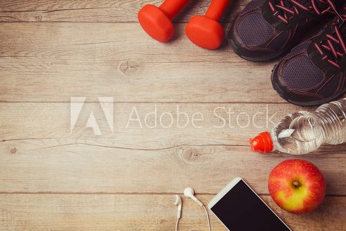 Fototapeta Fitness background with bottle of water, dumbbells and athletic shoes. View from above