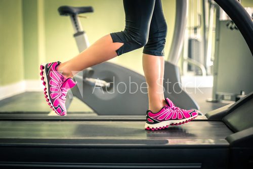Fototapeta Fitness girl running on treadmill. With muscular legs in gym.