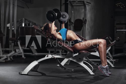 Fototapeta fitness girl training chest with barbell at gym