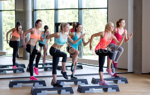 Fototapeta group of women working out with steppers in gym