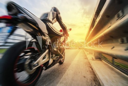 Fototapeta Moto da strada sfreccia vicino al guard rail al tramonto