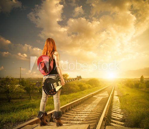 Fototapeta redhead woman with guitar at railway distance to sunset