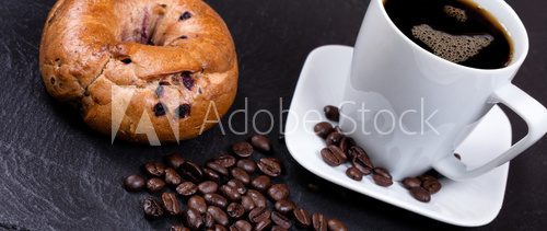 Fototapeta Roasted coffee beans with drink and bagel in background on slate