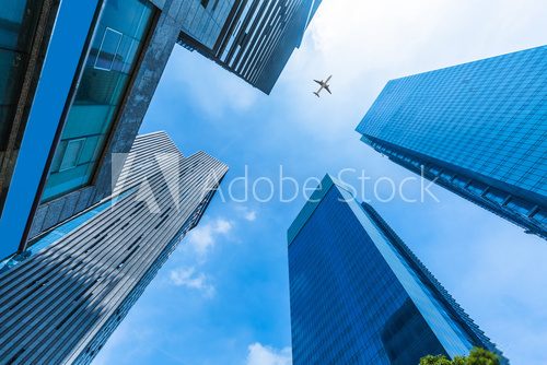 Fototapeta Skyscrapers with a flying airplane against blue sky.