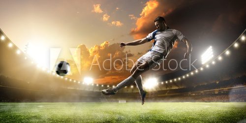 Fototapeta Soccer player in action on sunset stadium panorama background