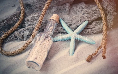 Fototapeta starfish, souvenir bottle and fishnet on the sand