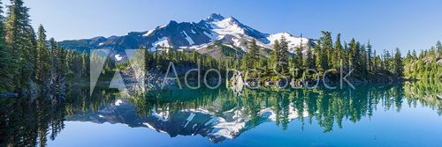 Fototapeta Volcanic mountain in morning light reflected in calm waters of lake.