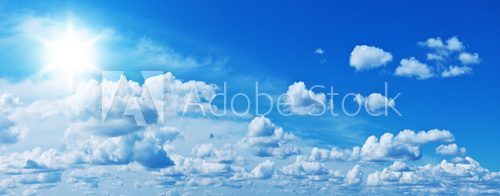 Fototapeta White heap clouds and bright sun in the blue sky.