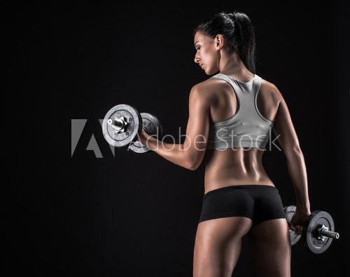 Fototapeta Young woman lifting the dumbbells